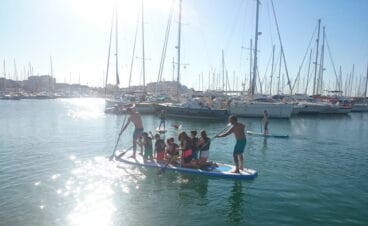 grupo de ninos sobre una tabla de paddle surf en el puerto de denia
