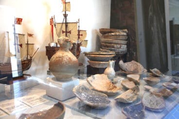 Jarrones y trozos de vajilla frente a reproducciones de las naves La Pinta, La Niña y Santa María