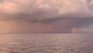 Un velero hacia el arcoíris en el horizonte