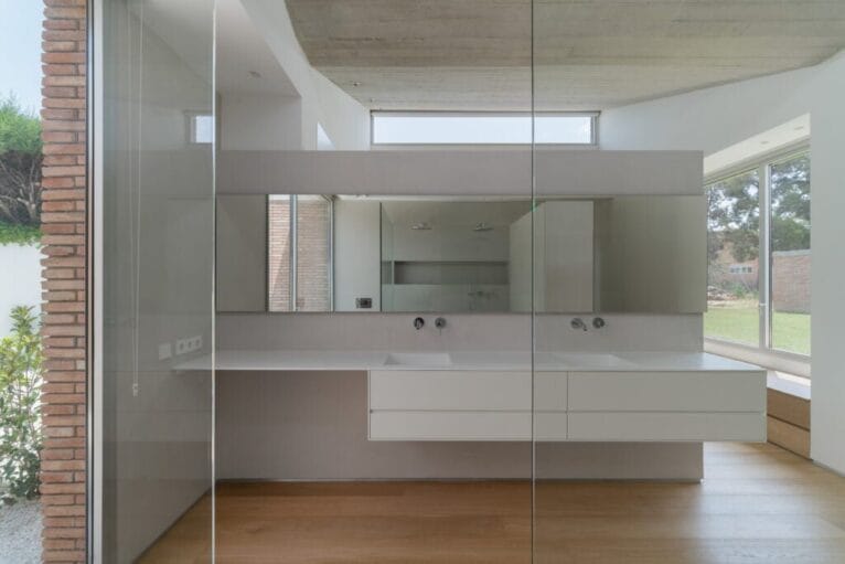 Baño luminoso con paredes de microocemento y muebles del lavabo en color blanco