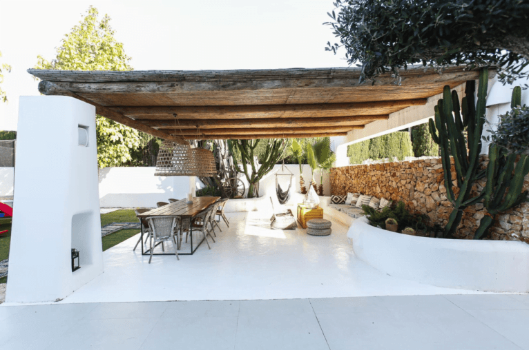 Zona de terraza cubierta en el jardín de estilo boho, con cactus y mesa de madera y una zona chill out