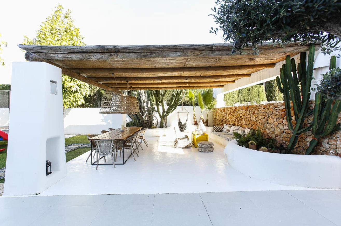 Zona de terraza cubierta en el jardín de estilo boho, con cactus y mesa de madera y una zona chill out