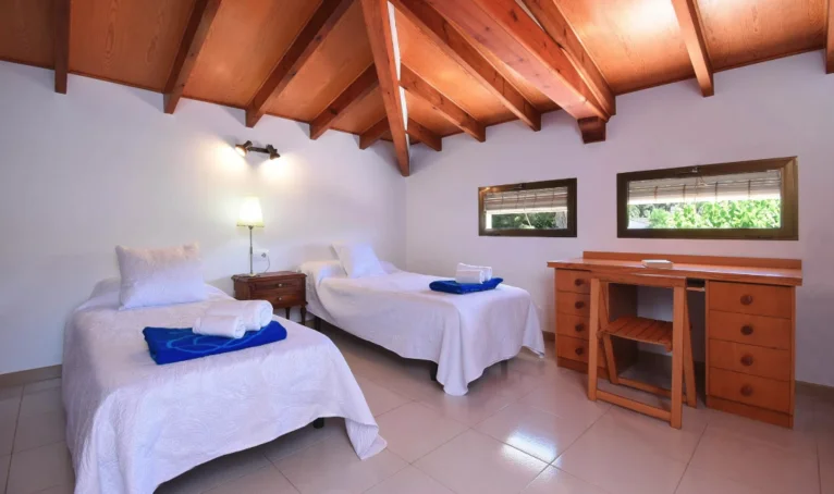 Деревенская спальня с деревянным потолком и двумя односпальными кроватями