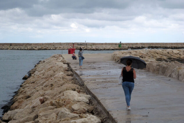 Imagen: Gente con paraguas paseando por una escollera de Dénia