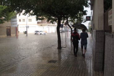 jovenes bajo el paraguas junto a una avenida anegada de denia durante un episodio de lluvia torrencial