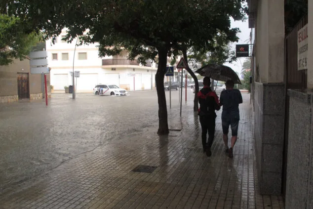La AEMET activa la alerta naranja en Dénia: ¿cómo afectará al fin de semana? 1 Imagen: Jóvenes bajo el paraguas junto a una avenida anegada de Dénia durante un episodio de lluvia torrencial