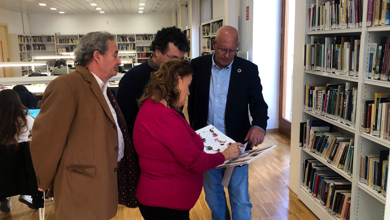 Grimalt, García de la Reina y los representantes de la asociación ojeando uno de los ejemplares de la Biblioteca
