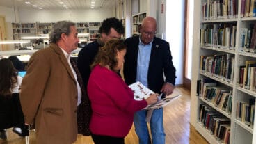 grimalt garcia de la reina y los representantes de la asociacion ojeando uno de los ejemplares de la biblioteca