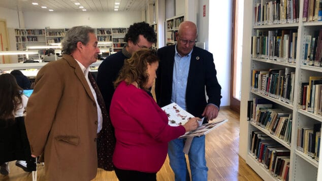 grimalt garcia de la reina y los representantes de la asociacion ojeando uno de los ejemplares de la biblioteca
