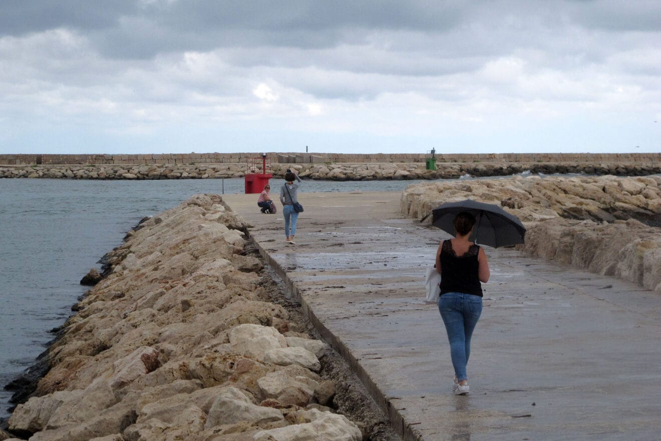 Gente con paraguas paseando por una escollera de Dénia