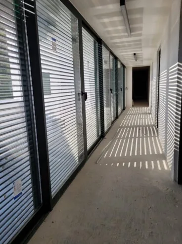 Pasillo acristalado con lamas, donde la luz dibuja sombras sobre el suelo