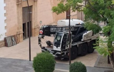 La grúa de gran tonelaje posicionada frente a la iglesia, lista para iniciar el delicado %22viaje%22 de los bronces hacia el suelo