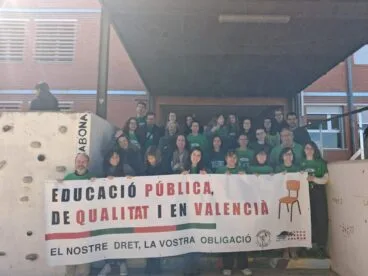 Grupo de docentes del IES Historiador Chabàs sosteniendo una pancarta por la educación pública, de calidad y en valenciano frente al instituto.