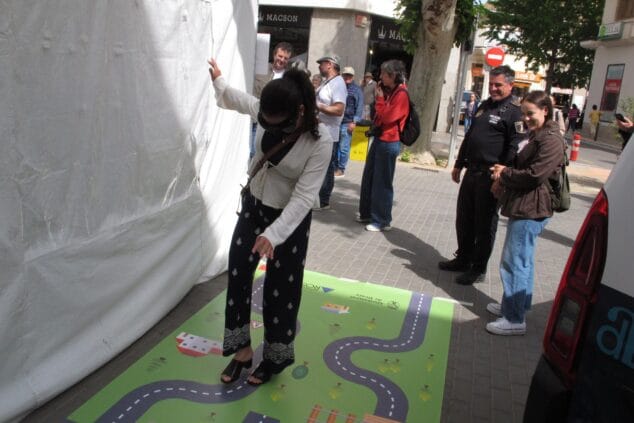Imagen: Joven con gafas de simulación sobre una alfombra de seguridad vial en la Fira de l'Estudiantat de Dénia, observada por un policía.