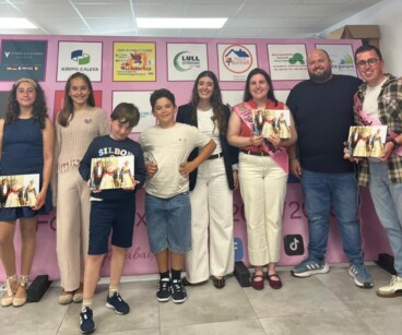 Grupo de personas de la Falla Baix la Mar posando con álbumes de fotos frente a un photocall.