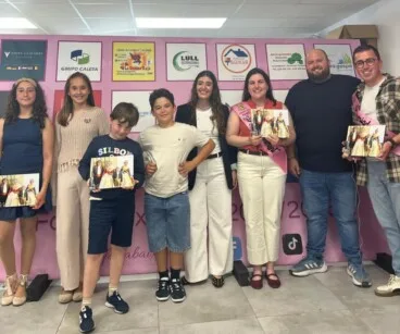 Grupo de personas de la Falla Baix la Mar posando con álbumes de fotos frente a un photocall.