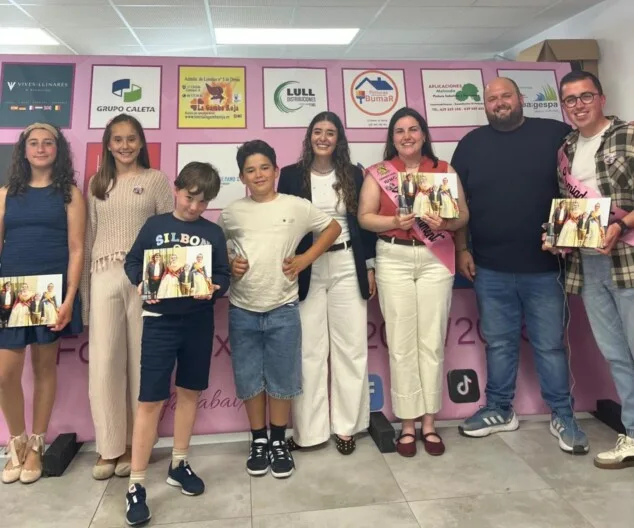 Grupo de personas de la Falla Baix la Mar posando con álbumes de fotos frente a un photocall.