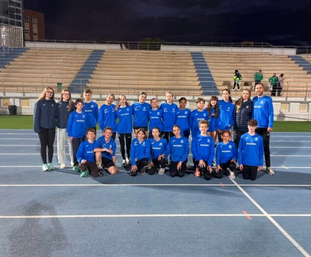 Imatge: Grup de joves atletes i entrenadors del Club d´Atletisme Baleària Diànium posant amb equipació blava en una pista d´atletisme.