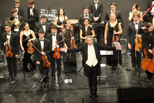 Imagen: El director de orquesta Pere Molina, con los brazos abiertos, saluda al público delante de la Orquesta de Cámara de Valencia en un escenario.