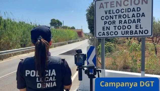 Ein örtlicher Polizist aus Dénia steht mit dem Rücken zur Kamera neben einem Stativ mit einem Geschwindigkeitsradargerät auf einer Straße.