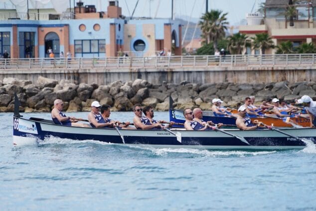 Imagen: Varios botes de remo con tripulaciones compitiendo intensamente en la regata final de la Liga Suma en Denia, cerca de un espigón.