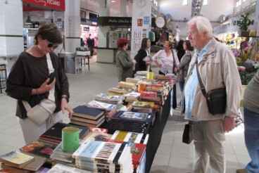 Vecinos de la localidad consultan los ejemplares disponibles en el stand solidario del Mercat Municipal de Dénia