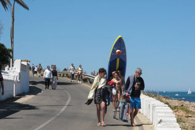 Bild: Besucher mit Stühlen und Paddle-Surfbrettern spazieren entlang der Zugänge zur Küste von Dénia inmitten des massiven Touristenandrangs.