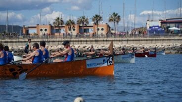 Embarcaciones de remo, una en primer plano con el dorsal 25 y el texto 'LIGA SUMA', compitiendo en la regata de Dénia con público al fondo.