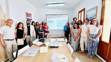 El Ayuntamiento de Dénia mueve ficha para desatascar las licencias urbanísticas 2 Foto de grupo de asistentes a una reunión de trabajo alrededor de una mesa. Al fondo, una pantalla de proyección muestra la diapositiva "Plan Conecta Urbanismo Dénia".