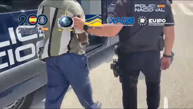 La red que inundaba España con camisetas falsas del Mundial 2026 tenía una base logística en Dénia 2 Imagen: Agente de la Policía Nacional escoltando a una persona detenida, con las manos esposadas, durante una intervención