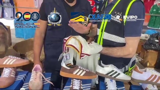 La red que inundaba España con camisetas falsas del Mundial 2026 tenía una base logística en Dénia 3 Imagen: Agentes de policía inspeccionando puestos de venta ambulante en un mercadillo, examinando prendas de ropa y calzado deportivo