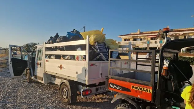 Imagen: Camión blanco de la empresa PAVASAL lleno de bolsas de basura negras y amarillas, y un vehículo utilitario naranja, estacionados en una playa de piedras.