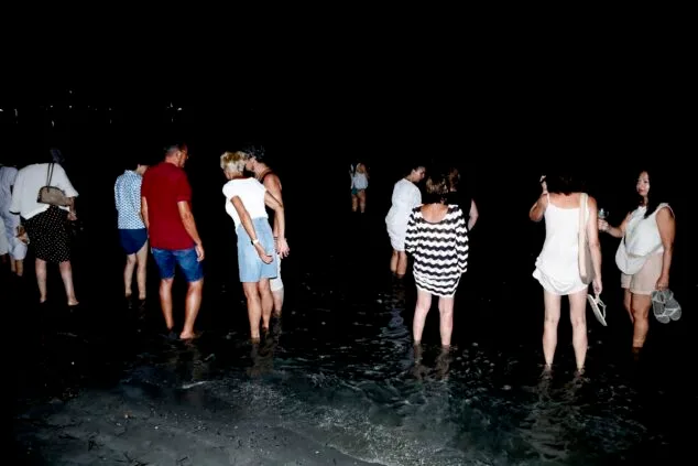 Grupo de personas de pie en la orilla del mar de noche durante la celebración de San Juan en Dénia.