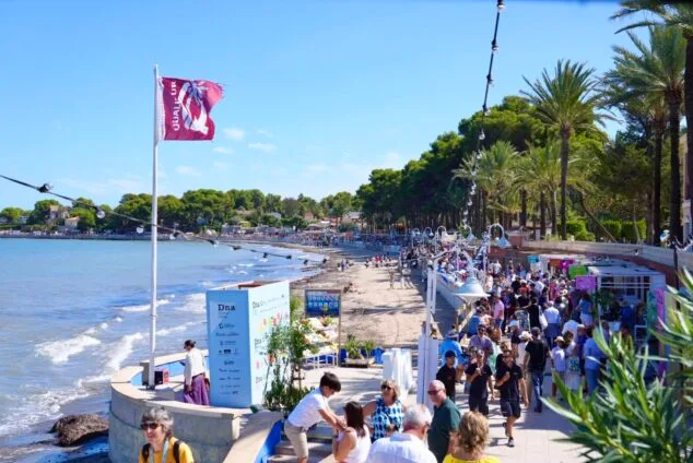 Imagen: Multitud de personas paseando entre puestos y banderas a lo largo del paseo marítimo durante el D*na Festival Dénia.