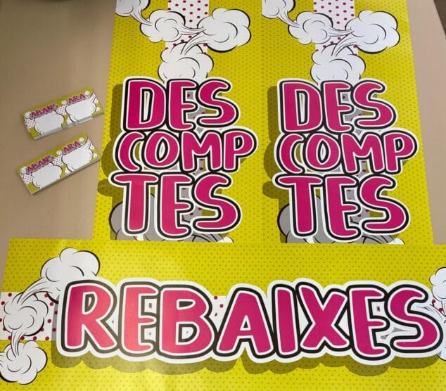 Dénia lanza una campaña para impulsar el valencià en el comercio durante las rebajas 3 Imagen: Fotografía de carteles grandes y etiquetas pequeñas con los textos 'REBAIXES' y 'DESCOMPTES' en estilo cómic sobre fondo amarillo con lunares.