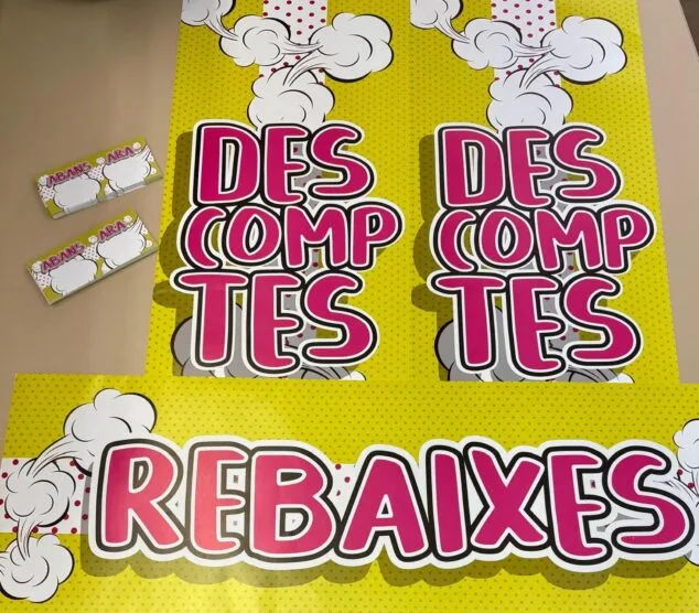 Imagen: Fotografía de carteles grandes y etiquetas pequeñas con los textos 'REBAIXES' y 'DESCOMPTES' en estilo cómic sobre fondo amarillo con lunares.