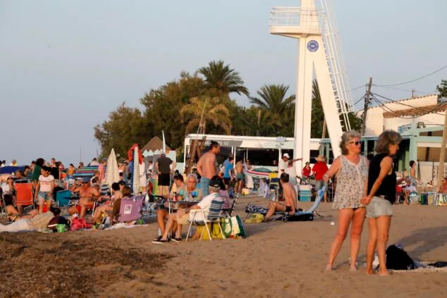 Playa de Dénia llena de gente y sombrillas al atardecer.