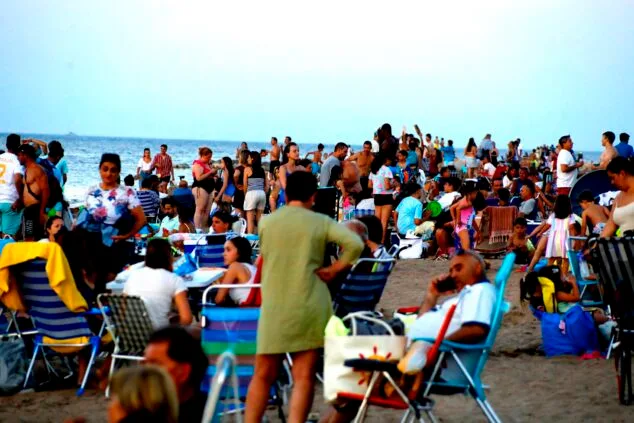 Imagen: Vista de una playa de Dénia llena de gente, sillas y neveras durante la tarde-noche.