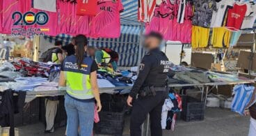 Agentes de la Policía Nacional y Policía Local de Denia inspeccionando ropa y camisetas de fútbol en un puesto de mercadillo.