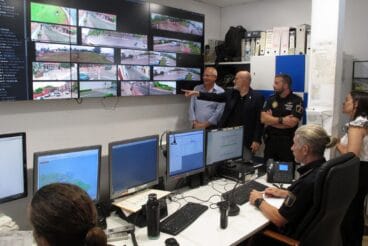 Dénia revoluciona su seguridad con un nuevo sistema de cámaras con inteligencia artificial 3 Autoridades y policías en el centro de control de Dénia observando una gran pantalla con múltiples imágenes del sistema de cámaras de seguridad, mientras un hombre señala una de las vistas.