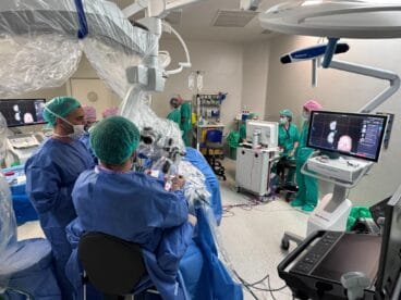 Equipo médico en quirófano realizando una neurocirugía con microscopio y monitores de visualización.