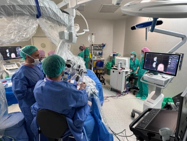 Equipo médico en quirófano realizando una neurocirugía con microscopio y monitores de visualización.