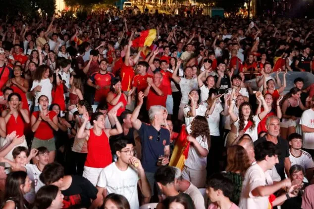 Multitud de aficionados con camisetas rojas y banderas de España animando en un evento nocturno al aire libre en Dénia.