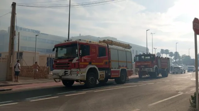 Declarado un incendio de vegetación en Dénia que moviliza a un amplio dispositivo de emergencias 6 Imagen: Dos camiones de bomberos del Consorcio Provincial de Alicante estacionados en una calle de Dénia, con el hospital HCB al fondo.