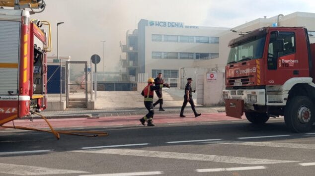 Declarado un incendio de vegetación en Dénia que moviliza a un amplio dispositivo de emergencias 3 Imagen: Camiones de bomberos de la Diputación de Alicante y personal de emergencias en una calle próxima al Hospital HCB Dénia, con humo visible en el fondo por un incendio.