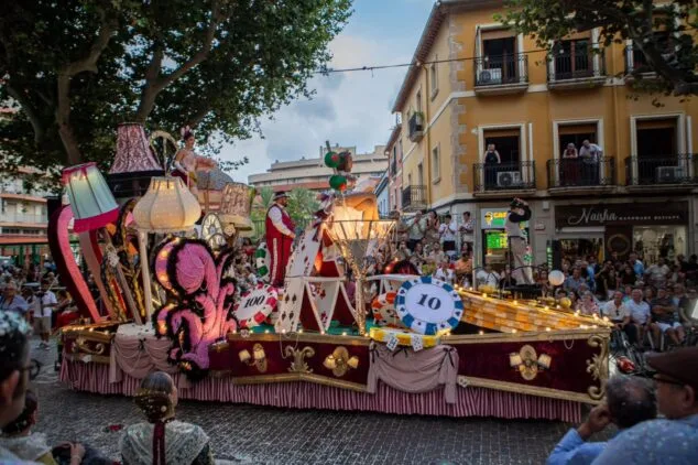 Carrossa de temàtica cabaret amb figures de cartes i fitxes de la Falla Baix la Mar desfilant en la Festa Major de Dénia, amb gent mirant des de balcons i carrer.