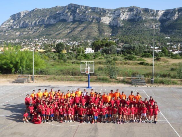 El Campus de Verano del Dénia Bàsquet Club clausura su XVII edición con 127 jóvenes y un balance muy positivo en Dénia 2 Imagen: Gran grupo de niños con camisetas rojas y adultos con camisetas naranjas posando en una pista de baloncesto exterior.