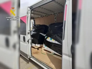 Intervenidas más de mil botellas de «gas de la risa» en el puerto de Dénia 13 Vista del interior de una furgoneta blanca cargada con palés de cajas que contienen botellas de óxido nitroso, con el logotipo de la Guardia Civil en la esquina superior izquierda.