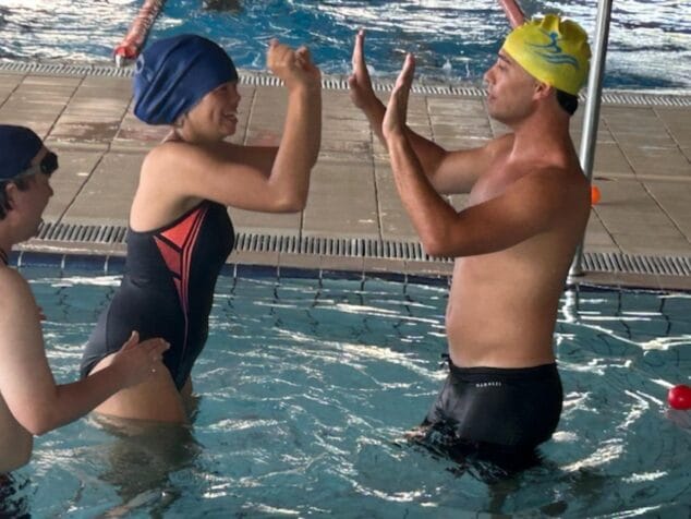 Condenados al Bordillo arranca su escuela de verano inclusiva con más de 50 participantes 6 Imagen: Dos personas chocan las manos alegremente dentro de una piscina durante una actividad de verano.