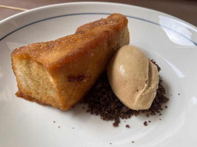 Plat de postres amb una peça caramel·litzada, una quenelle de gelat i terra de xocolata.